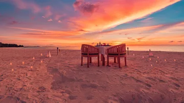 activity, sunset - Un tavolo per due allestito sulla sabbia per una cena romantica, sotto un cielo al tramonto dai colori vivaci.