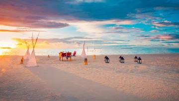 activity, beach, luxury, sunset - Un tavolo apparecchiato per una cena romantica privata su una spiaggia di sabbia bianca con lanterne al tramonto.