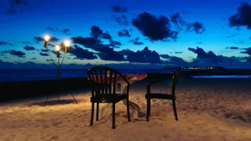 activity, beach, relax, sunset - Un tavolo romantico per due apparecchiato sulla spiaggia al crepuscolo con torce accese sotto un cielo blu profondo.