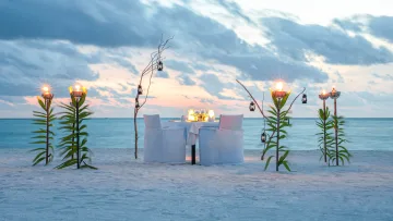 activity, sunset - Un tavolo privato apparecchiato per due su una spiaggia di sabbia al tramonto, illuminato da torce e lanterne.