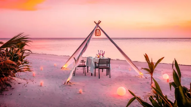 activity, relax, sunset - Un tavolo per una cena romantica privata allestito sulla spiaggia tropicale sotto un arco decorativo al tramonto.
