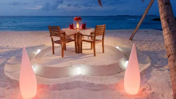 activity - Un tavolo apparecchiato romanticamente per due su una spiaggia sabbiosa al crepuscolo, illuminato da lanterne.