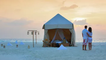 activity, luxury, relax, sunset - A loving couple stands before a luxury tent set up for an overnight stay on a private sandbank at sunset.