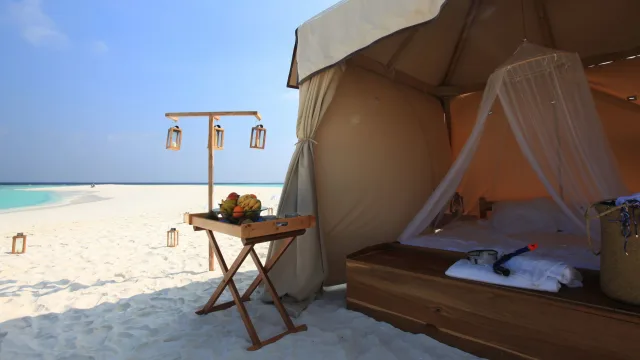 activity, accommodation, beach, luxury, relax - A luxurious tent set up for an overnight stay on a tropical sandbank featuring a cozy bed and fresh fruit platter.