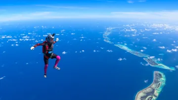 activity, sky - Un paracadutista in caduta libera contro un cielo blu intenso con una vista aerea mozzafiato degli atolli tropicali.