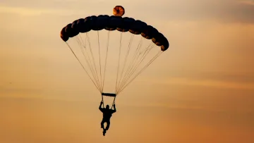 activity, sky, sunset - Silhouette di un paracadutista con paracadute aperto che fluttua nel cielo dorato durante un tramonto tropicale