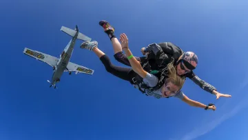 activity, sky - Una persona si gode un salto in tandem con un istruttore contro un cielo azzurro, con aereo da lancio nelle vicinanze.