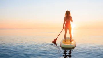 activity, sea, sunset - Donna in piedi su una tavola da stand up paddle nell'oceano durante un tramonto dorato, godendosi l'attività in mare.