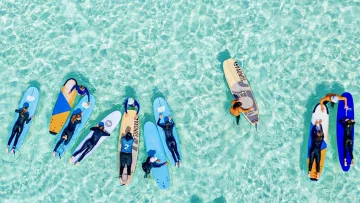 activity, sea - Aerial view of a group of students practicing surfing on colorful boards in the crystal clear turquoise ocean water