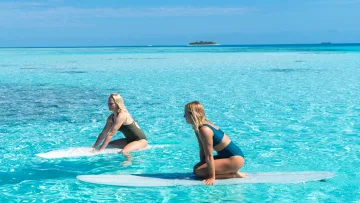 activity, sea - Two women kneeling on surfboards in the crystal clear turquoise shallow waters of a tropical island lagoon.