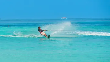 activity, sea - Un uomo con giubbotto salvagente si diverte durante una energica sessione di wakeboard sulle acque turchesi limpide.