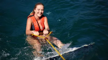 activity - Una donna gioiosa con giubbotto salvagente arancione che pratica wakeboarding nelle limpide acque blu delle Maldive.