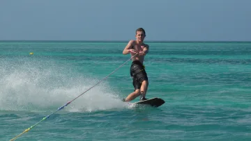activity - Un giovane uomo si diverte facendo wakeboarding sulle acque turchesi di un'isola tropicale, creando spruzzi d'acqua.