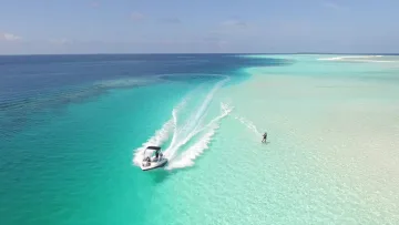activity, sea - Aerial view of a person waterskiing behind a fast speed boat in the turquoise lagoon of a beautiful tropical island.