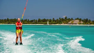 activity, people, sea - A smiling woman in a life vest enjoying water skiing on the turquoise ocean water of a tropical island resort.