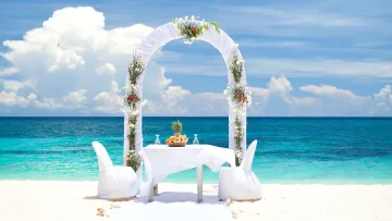 activity, beach - A beautiful white floral wedding arch with a table for two on a pristine white sand beach overlooking the turquoise ocean.