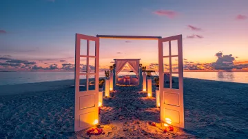 activity, beach, sunset - A beautiful wedding ceremony setup with white doors and glowing lanterns on a sandy beach at a colorful sunset.