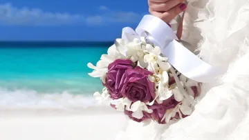 activity, beach, people - Close up of a bride holding a beautiful floral bouquet with purple roses and white orchids on a sandy beach.