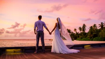 activity, people, sunset - A newlywed couple holding hands on a wooden jetty at sunset during a romantic wedding ceremony on a tropical beach.