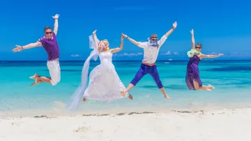 activity, beach, people - Happy bride and groom jumping with friends on a tropical white sand beach under a bright blue sky in the Maldives.