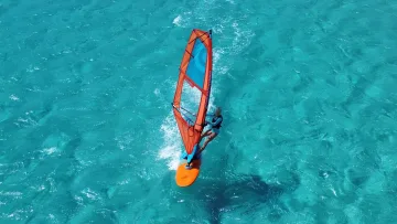 activity, sea - Vista aerea di una bambina che fa windsurf con una vela arancione sulle acque turchesi della laguna tropicale.