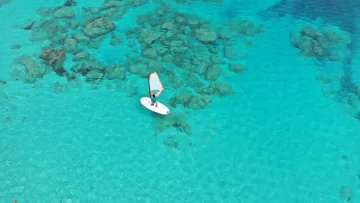 activity, drone-shot, sea - Vista aerea di un windsurfer che naviga su una tavola bianca con vela arancione nella laguna turchese brillante.