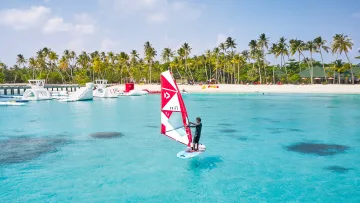 activity, sea - Un windsurfista scivola sulle acque turchesi e cristalline di un'isola maldiviana vicino a un parco acquatico.