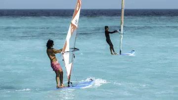 activity, sea - Due persone fanno windsurf su tavole nell'acqua cristallina color turchese dell'oceano sotto un cielo azzurro terso.