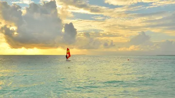 activity, sea, sunset - Un windsurfer scivola sulle calme acque turchesi dell oceano sotto un drammatico cielo dorato al tramonto con barca.