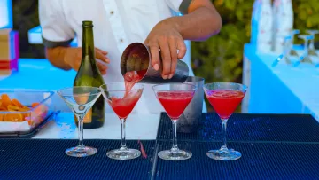 resort - Un barman professionista versa un cocktail rosso brillante nei bicchieri da martini da uno shaker in un bar di resort.