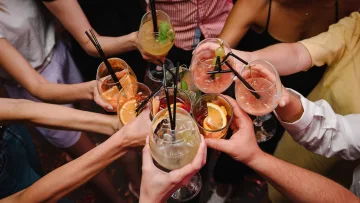 people - Gruppo di amici che brinda con cocktail colorati decorati con frutta e cannucce durante un aperitivo al tramonto.
