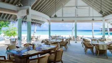 facilities, luxury, resort - Un elegante ristorante all'aperto con tavoli in legno e sedie in vimini affacciato su una spiaggia bianca e oceano blu.