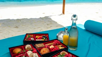 beach, food, luxury, relax - Elegant breakfast boxes with tropical fruits and pastries on a blue sunbed overlooking a pristine white sand beach.