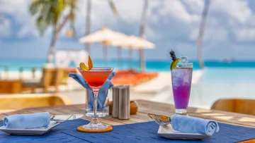 resort, sea - Due cocktail colorati, uno rosso e uno viola, serviti su un tavolo del ristorante che affaccia su una spiaggia tropicale.