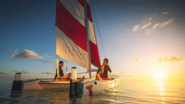 activity, people, relax, sea, sunset - A romantic couple sailing on a catamaran across calm tropical waters during a beautiful golden sunset hour view.
