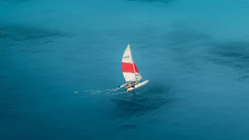 activity, drone-shot, sea - Aerial perspective of a small catamaran with a red and white sail navigating the calm turquoise Indian Ocean water