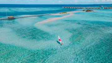 activity, drone-shot, resort, sea - Aerial view of a small red and white catamaran sailing through the crystal clear turquoise water of a resort lagoon