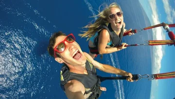 activity, people, sea - Happy couple wearing sunglasses captured in a selfie while parasailing high above the deep blue ocean waters.