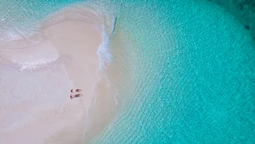 beach, drone-shot, people, relax, sea - Aerial view of a couple sunbathing on a white sandy sandbank surrounded by vibrant turquoise crystal clear water