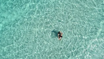 drone-shot, people, sea - Aerial view of a young couple embracing and swimming in shallow, transparent turquoise water in the tropics.