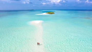 drone-shot, nature, people, sea - Aerial view of a couple holding hands walking along a white sandbank in crystal clear turquoise lagoon water.