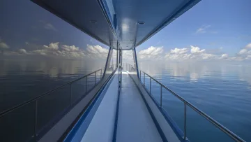 activity - Ponte laterale di una barca che naviga sull'oceano calmo blu, che riflette il cielo con le nuvole, creando un'atmosfera serena.