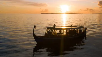 activity, sea, sunset - Silhouetted traditional Maldivian Dhoni boat on calm ocean waters during a breathtaking golden hour sunset view.