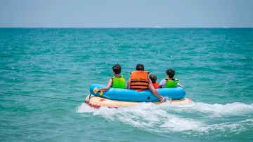 activity, people, sea - Una famiglia di quattro persone con giubbotto salvagente si diverte su un tubo gonfiabile blu e giallo sull'oceano.
