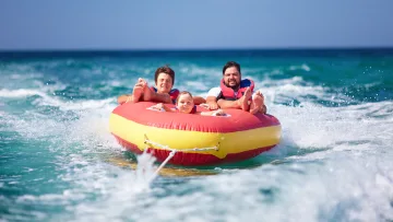 activity, people, sea - Padre felice e due bambini su un gommone rosso e giallo trainato nell oceano blu indossando giubbotti di salvataggio