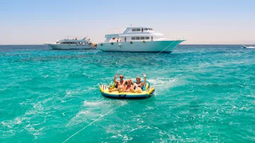 activity, people - Una famiglia felice di tre persone saluta mentre cavalca un gommone trainato da un motoscafo in mare aperto