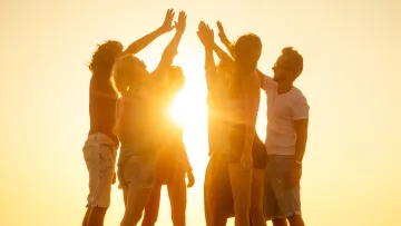 beach, people, relax, sunset - Group of young friends standing on a sandy beach, silhouetted against a golden sun while giving each other a high five.