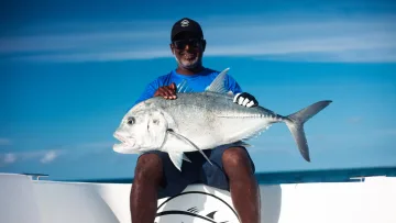 activity, animal, people, sea - A smiling local fisherman holding a large giant trevally fish while sitting on the deck of a boat in the open ocean.