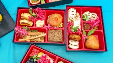 food - Assortment of gourmet bento boxes filled with fresh fruits, pastries, sandwiches, and snacks on a bright blue cloth.