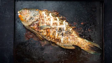 food - A delicious whole grilled reef fish seasoned with herbs and spices, served on a rustic dark metal baking tray.
